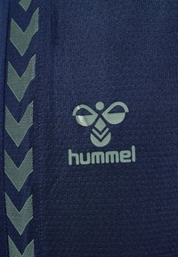 Prodotto Hummel con un tessuto texturizzato blu navy. Presenta un logo verde e dettagli a motivi a zigzag lungo il lato.