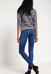 Suéter de estampado de leopardo gris con mangas largas, combinado con jeans ajustados azules. La textura parece suave; los jeans tienen bolsillos traseros y un ligero estiramiento.