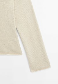 Manche longue de pull en maille crème avec texture côtelée visible sur fond blanc.