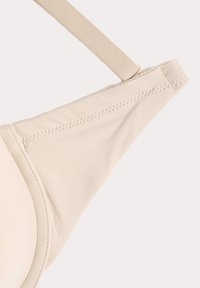 Beige beha van zacht materiaal, met gevormde cups en verstelbare bandjes. Beschikt over soepele stiksels en een naadloos ontwerp voor een nette uitstraling.