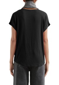 Camisetta nera a maniche corte con texture a coste, scollatura rotonda e orlo curvo, abbinata a pantaloni grigi a gamba larga.