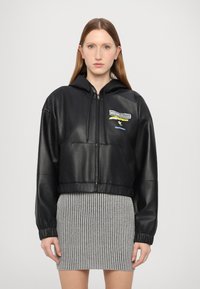 Schwarze, kurze Lederjacke mit Kapuze, mit einem Reißverschluss und besticktem Logo-Detail. Glatte Oberfläche und lässiger Schnitt.