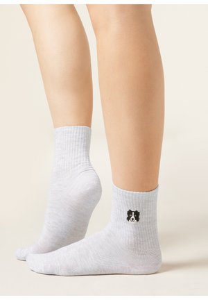 Nogi w jasnoszarych prążkowanych skarpetkach, na jednej z nich, blisko kostki, wyhaftowana jest mała czarno-biała twarz psa.