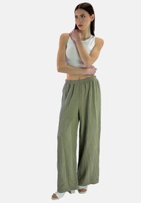 Lätta, texturerade, olivgröna byxor med vida ben och elastisk midja, kombinerat med en åtsittande vit ärmlös topp och vita blockklackssandaler.