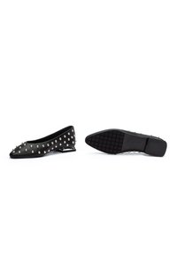 Des ballerines noires à bout pointu ornées de clous argentés sur le dessus et de petits talons décoratifs argentés, montrées de côté et en vue de la semelle.