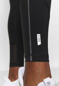 Zwarte sportleggingen met een lengte tot halverwege het scheenbeen, witte logoaccenten en contrasterende stiksels. Glad textuur met een aansluitend ontwerp.