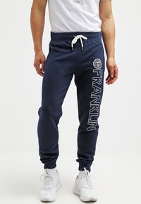 Marina sweatpants med dragsko i midjan, sidofickor och vit textdesign "FRANKLIN", kompletterad med en rund logotypapplikation på höften.