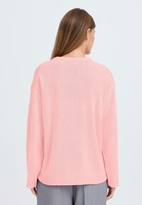 Ljust rosa tröja med avslappnad passform, ribbade manschetter och nederkant, samt ett mjukt, strukturerat stickat material. Bakdelen har en enkel, rundad halsringning.