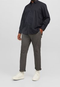 Camisa de botones azul oscuro, pantalones grises y zapatillas blancas. La camisa tiene cuello y mangas largas; los pantalones están enrollados en los puños.