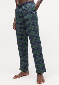 Kárované pohodlné nohavice s zeleno-námorníckym pruhovaným vzorom, so sťahovacím pásom a jemnou textúrou. Obsahuje malú kapsičku s logom.