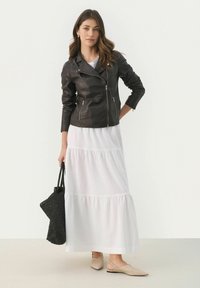 Giacca da motociclista in pelle nera con tasche con zip, vestito maxi bianco a strati, ballerine beige e borsa a tracolla nera intrecciata.