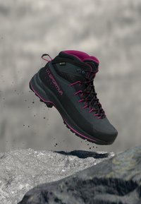 Bota de caminhada preta com detalhes em rosa, parte superior texturizada e sola de borracha. Apresenta um design de tornozelo alto, atacadores e um rótulo GORE-TEX.