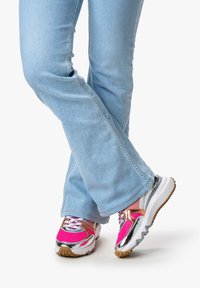 Scarpe sportive con tomaia in rete rosa, dettagli argentati e suola bianca texturizzata, abbinate a jeans svasati azzurri chiari.