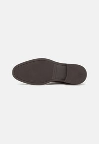 Semelle d'une chaussure habillée en cuir brun foncé avec une semelle texturée, un talon lisse et le nom de la marque "Tommy Hilfiger" embossé près de la voûte plantaire.