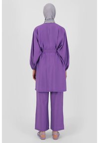 Purple two-piece outfit featuring a long, loose top with a tied belt and wide-leg pants. Material appears lightweight with a smooth texture.