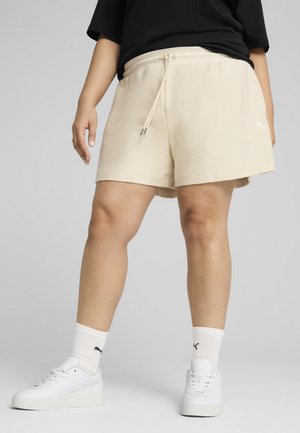 Shorts beige in tessuto con vita regolabile e tasche laterali, abbinati a sneakers bianche e calze bianche a coste.