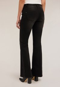 Schwarze Schlagjeans mit einer glatten Textur, ausgestattet mit Gesäßtaschen und einer mittelhohen Taille, kombiniert mit schwarzen Absatzstiefeln.