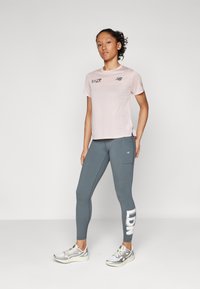 Rausvas New Balance marškinėliai trumpomis rankovėmis su logotipu. Pilkos legging'ės su šonine kišene ir tekstu "LDN". Pilkai balti bėgimo bateliai.