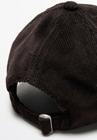 Cappellino da baseball in corduroy marrone con cinturino posteriore dotato di una fibbia di regolazione in metallo argentato e una superficie testurizzata e rigata.