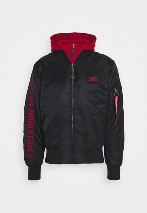 Crna bomber jakna s crvenom kapuljačom, s logotipom "Alpha Industries" u crvenoj boji na rukavu, zatvorenim džepovima i rebrastim manžetama i donjim rubom.