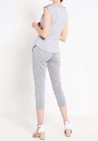 Top senza maniche grigio chiaro con spalle arrotondate e orlo leggermente svasato abbinato a pantaloni grigio chiaro taglio corto e sandali bianchi con tacco a blocco.