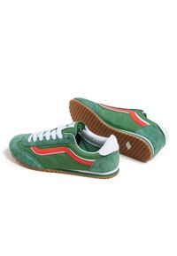 Green suede and textile sneakers with white laces, featuring a red accent stripe and a textured gum rubber sole.