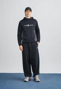 Black Nike Shox hoodie with gray side accents and logo, paired with black sweatpants and gray sneakers, set against a neutral background.