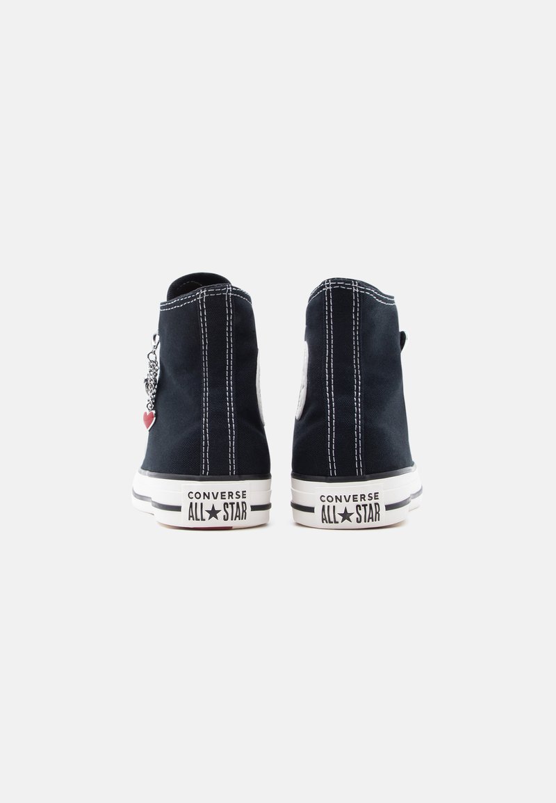 Sneakers alte in tela nera con cuciture bianche e suole di gomma. Presentano una toppa con il logo e un charm decorativo sul lato.