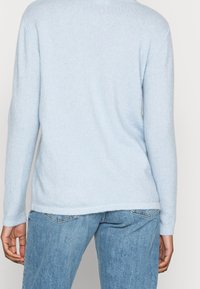 Pull bleu clair à manches longues avec une texture fine en maille, ourlet fini et encolure arrondie, associé à un pantalon en denim bleu clair.