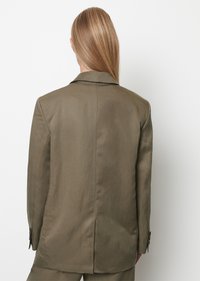 Olivově zelený blazer s jedním rozventilováním, vyrobený z hladkého materiálu. Obsahuje klopové límce a knoflíkové manžety, vytvarovaný pro přiléhavý vzhled.