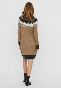 Robe pull en tan avec un empiècement noir et blanc à motifs. Manches longues avec des poignets foncés, texture côtelée, design longueur genou.