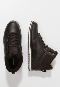 Un par de botas de invierno de cuero marrón oscuro con forro de piel, ojales metálicos y suelas de goma con borde blanco, una mostrada desde arriba y otra de lado.