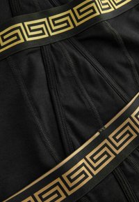 Schwarzer Stoff mit glatter Textur, der ein breites schwarzes Band mit einem goldenen geometrischen Muster über die Mitte aufweist.