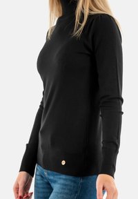 Maglione a collo alto nero realizzato in tessuto morbido. Presenta polsini e orlo a coste, con un piccolo dettaglio del logo metallico in basso. Design aderente.