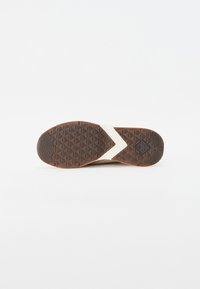 Brun gummislid med et tekstureret mønster, der har en hvid accentstribe og et geometrisk design på bunden for bedre greb.