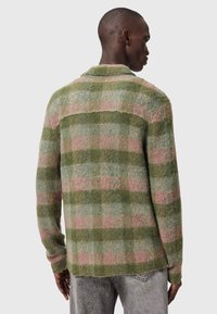 Πλεκτή ζακέτα από μάλλινο ύφασμα με καρό μοτίβο σε πράσινο και ροζ, με άνετη εφαρμογή, γιακά και φθαρμένες άκρες. Η πίσω όψη αποκαλύπτει υφασμένο μοτίβο.