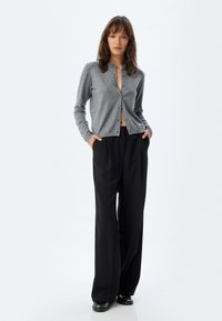 Cárdigan gris con cierre de botones, mangas largas y un corte relajado, combinado con pantalones negros de cintura alta y zapatos negros brillantes.
