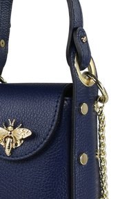 Marineblauwe leren handtas met een gestructureerd oppervlak, gouden bijenhardware detail en kettingaccenten. Voorzien van een flapsluiting en opvallende studs.