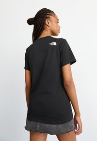 Tricou din bumbac negru, cu guler rotund, mânecă scurtă și un logo alb pe partea superioară a spatelui. Designul este simplu, cu o croială clasică.