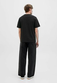 Schwarzes T-Shirt mit kurzen Ärmeln aus Baumwolle, mit lockerer Passform und Rundhalsausschnitt, kombiniert mit weit geschnittenen, dunklen Jeans und weißen Sneakers.