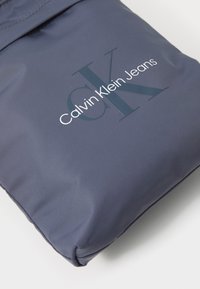 Borsa in tessuto blu scuro, con una finitura liscia e una texture pronunciata. Presenta un logo ben visibile: "Calvin Klein Jeans" con le iniziali stilizzate "CK."