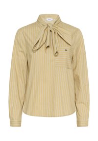 Blouse beige à manches longues avec des rayures verticales blanches, un grand nœud papillon au col et une poche plaquée boutonnée sur la poitrine.