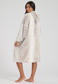 Manta con capucha hecha de tejido de felpa, que presenta un patrón de rayas de cebra en beige y blanco, manga larga y un ajuste relajado.