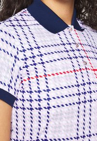 Kortärmad polo i ljusrosa med marinblå krage. Har ett geometriskt mönster i marinblått, grått och rött, med tre knappar på ståkragen.