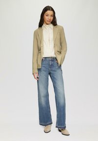 Lichtbeige blazer over een witte, gestreepte shirt; gecombineerd met wijde lichtblauwe jeans; beige enkellaarsjes; gladde textuur, op maat gesneden.