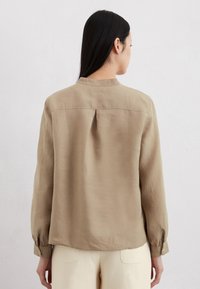 Hellbraunes Langarmhemd mit rundem Kragen, Rückenfalten-Detail und geknöpften Manschetten, aus einem glatten Stoff gefertigt.