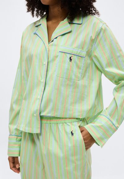 Γυναίκα που φοράει ανοιχτοπράσινο ριγέ πουκάμισο με κουμπιά και μακριά μανίκια και παντελόνι που ταιριάζει, με κεντημένο λογότυπο στην τσέπη και στο πόδι του παντελονιού.