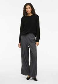 Maglione nero a maglia con un motivo texturizzato, abbinato a pantaloni grigi a vita alta e gamba larga e décolleté neri a punta.