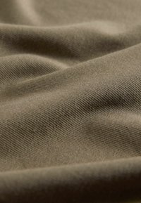 Țesătură kaki cu o textură moale, având un model subtil cu nervuri și mici pliuri, evidențiind caracteristicile sale ușoare și elastice.