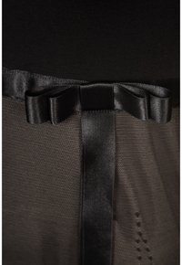 Détail d'un nœud en ruban de satin noir sur un tissu foncé texturé, avec une bande de satin verticale sous le nœud.